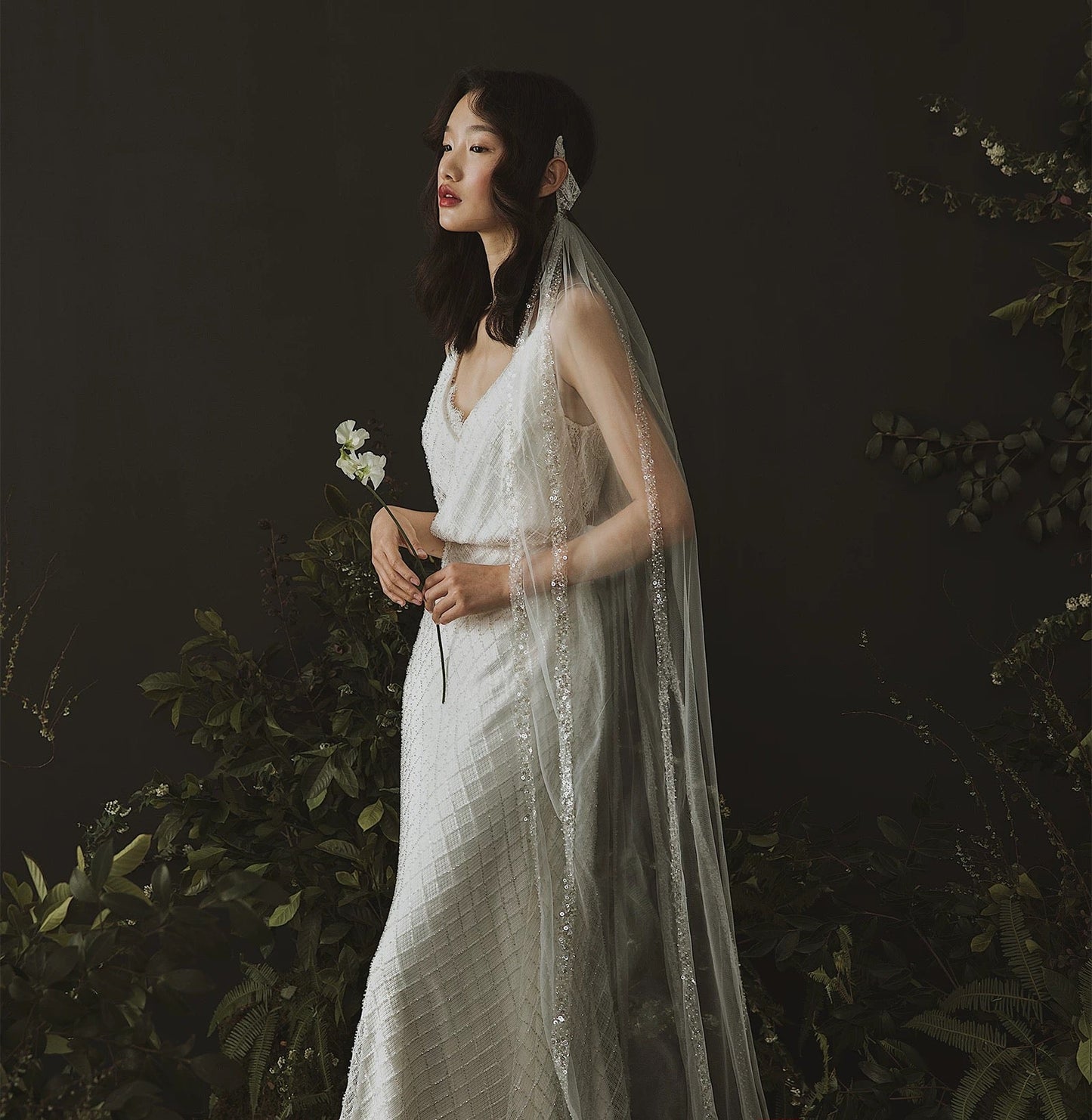Woman in a white wedding dress with a veil standing against a dark background with 'DEARWHITE' branding.