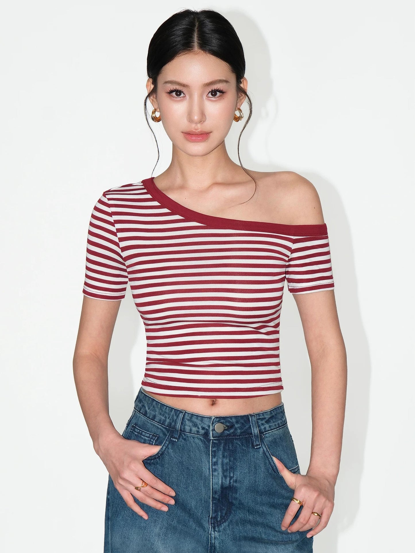 Woman wearing a red and white striped top with blue jeans on a plain background