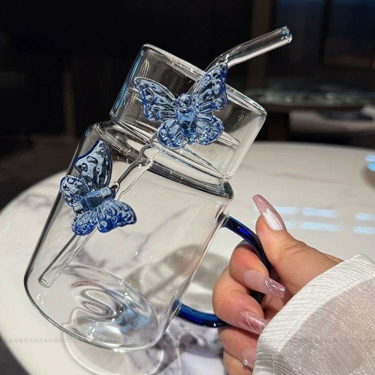 Clear glass mug with blue butterfly designs held by a hand on a blurred background
