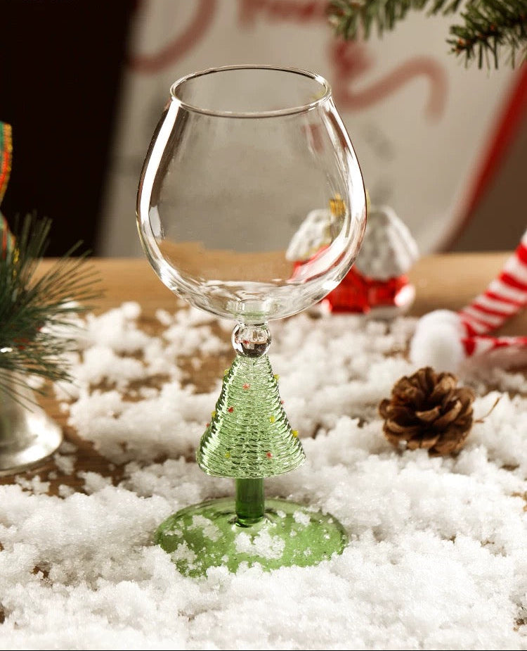 Clear glass wine glass with green base on a snowy surface, Christmas decorations in the background