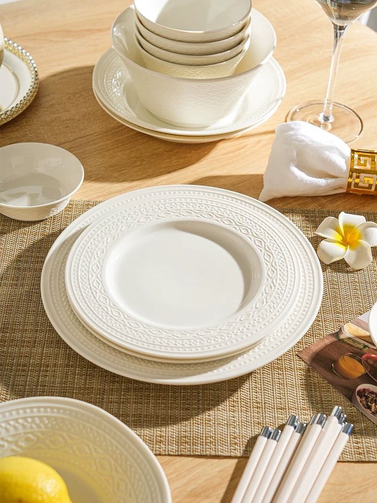 White ceramic dinnerware set on a wooden table with a woven placemat.