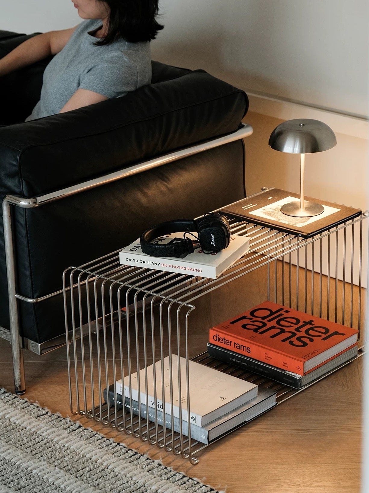 Modern living room with a black sofa and a metal side table holding books and a lamp.