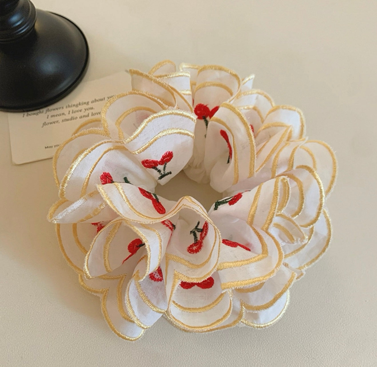 White floral scrunchie with red flowers and gold accents on a beige surface