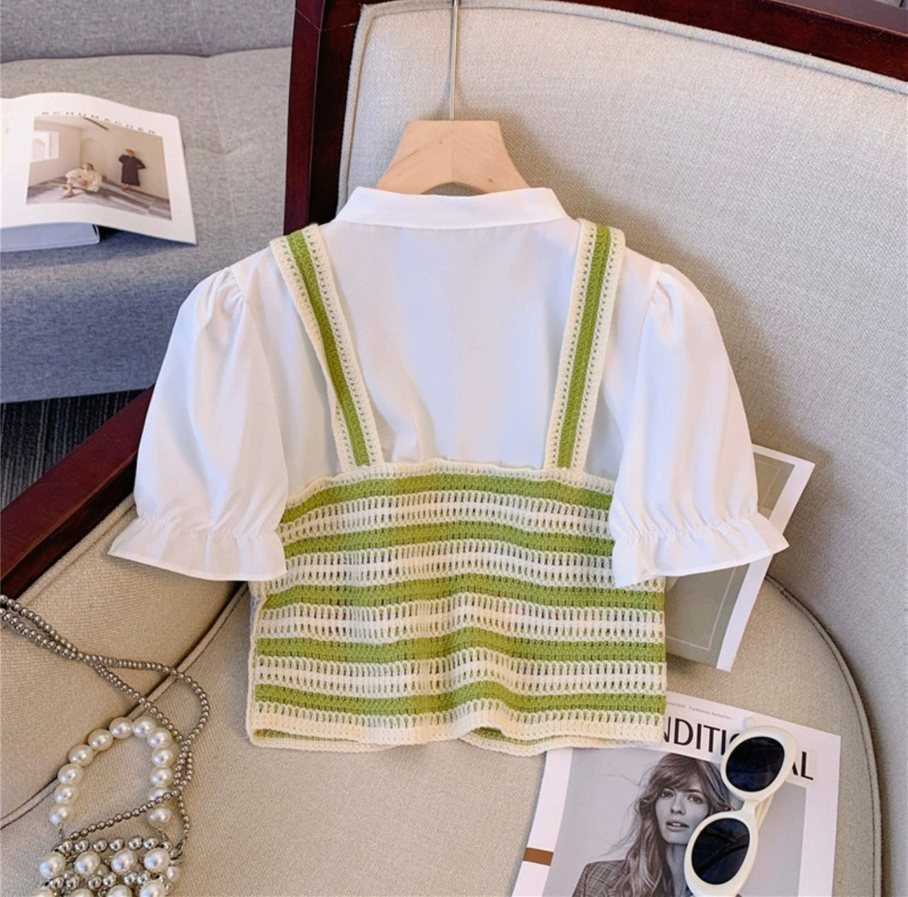 White blouse with green striped straps on a hanger against a neutral background