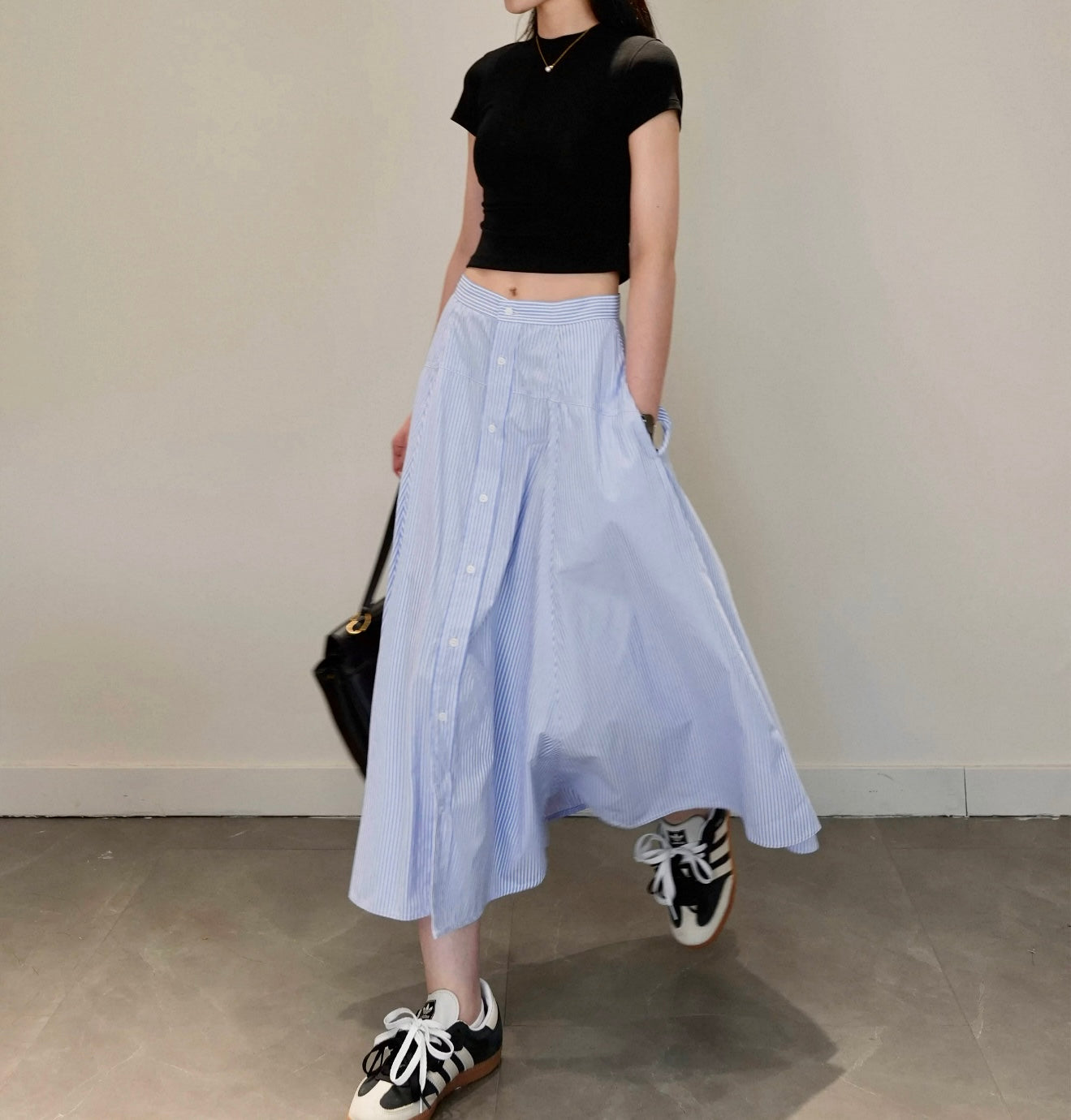 Person wearing a black crop top, light blue skirt, and black and white sneakers against a plain background.