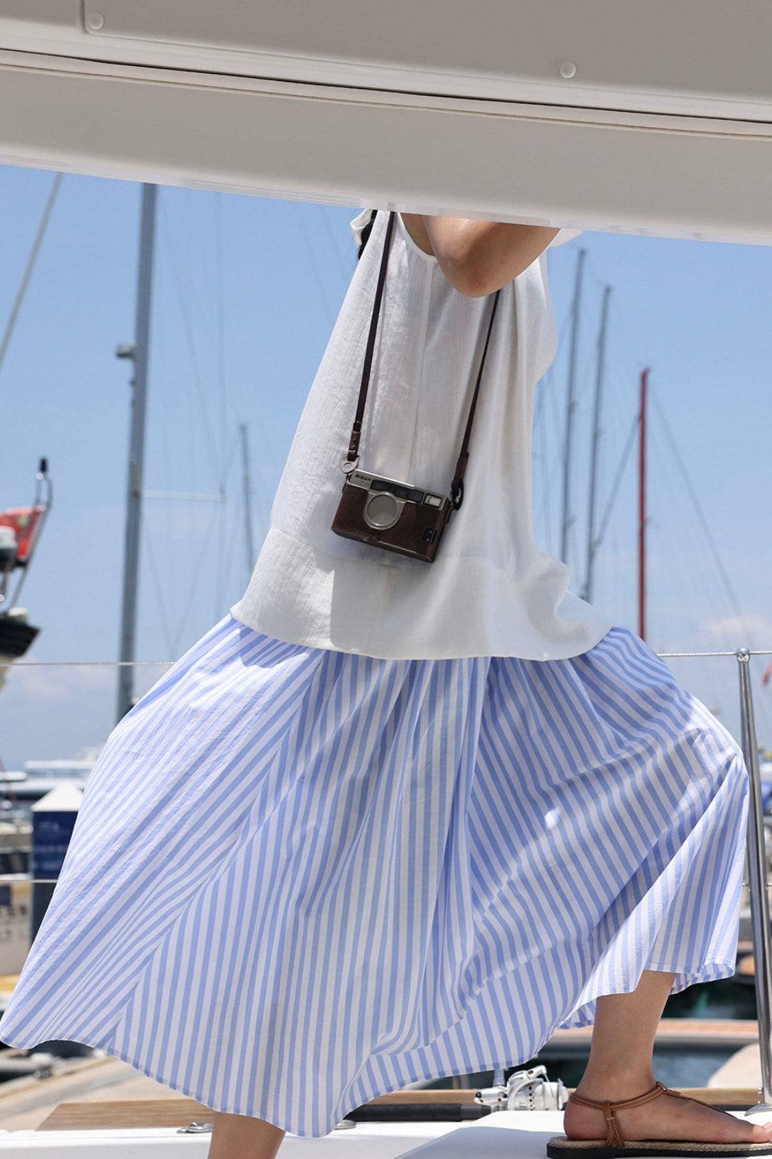 Person wearing a white shirt and blue striped skirt with a camera around their neck, standing on a boat.