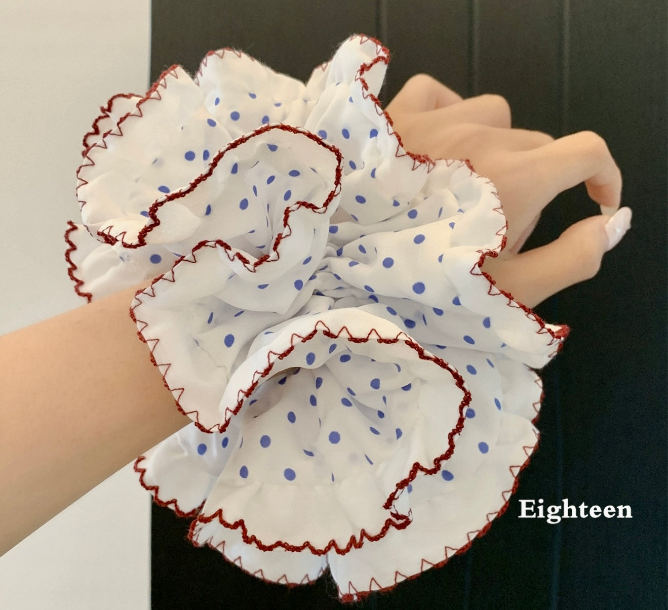 White fabric flower with blue polka dots and red trim held by a hand against a neutral background.