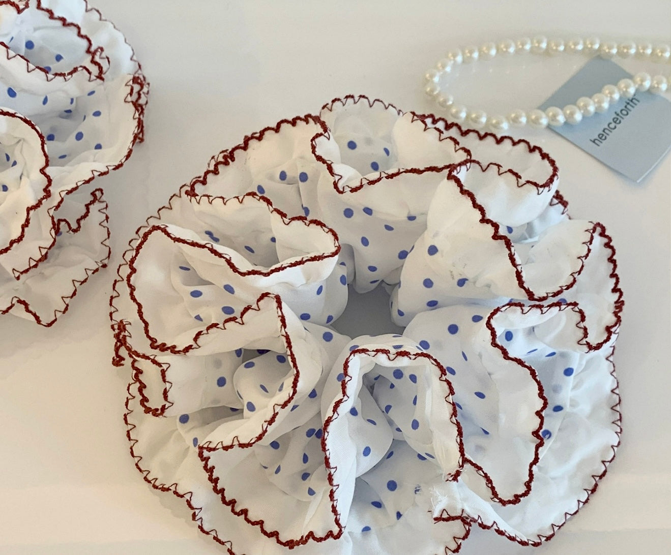 White scrunchie with blue polka dots and brown ruffled edges on a light background