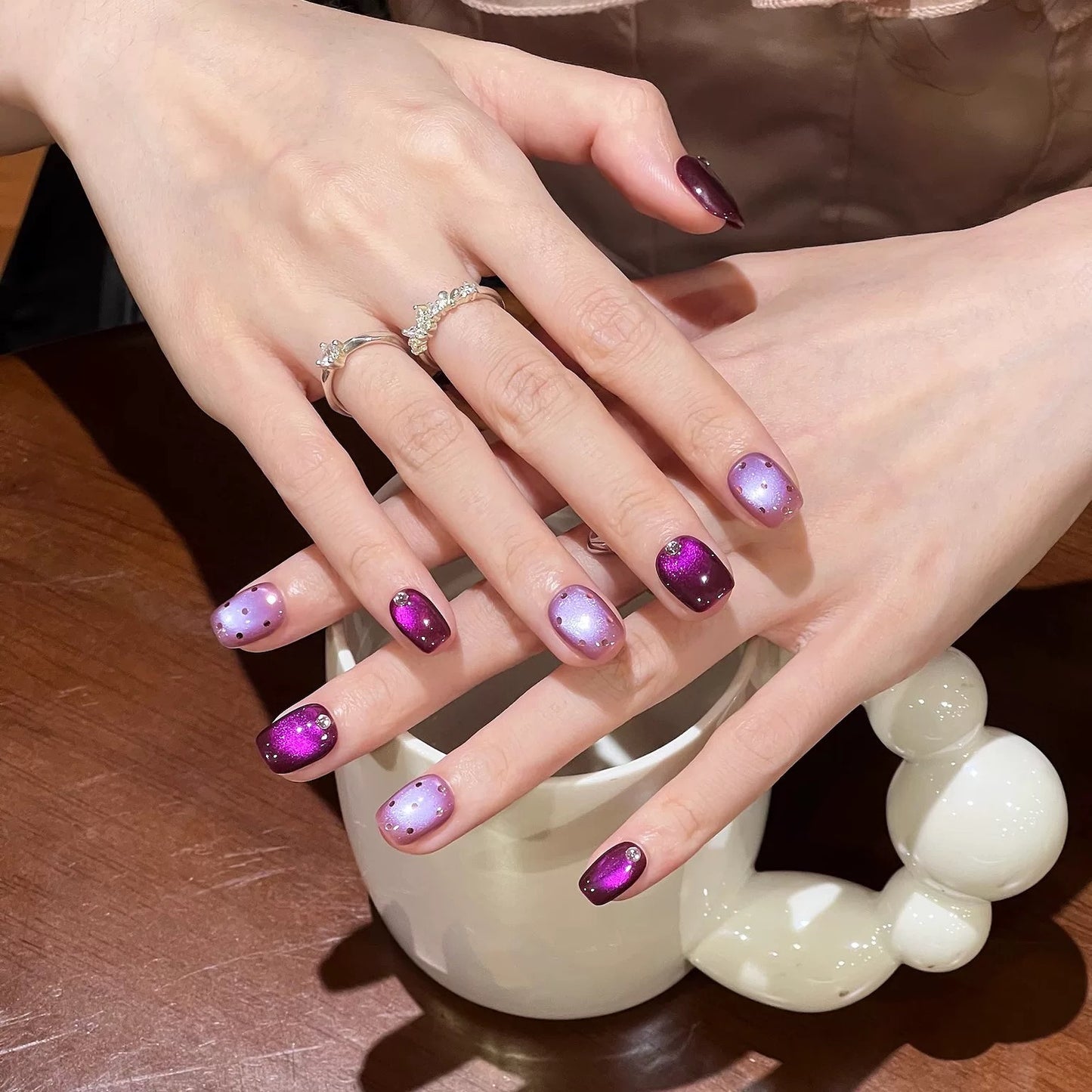 Close-up of hands with purple and pink nail polish holding a white ceramic cup.