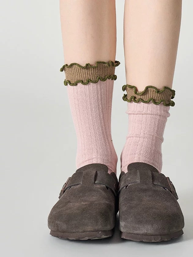 Pink socks with ruffled cuffs and brown loafers on a light gray background