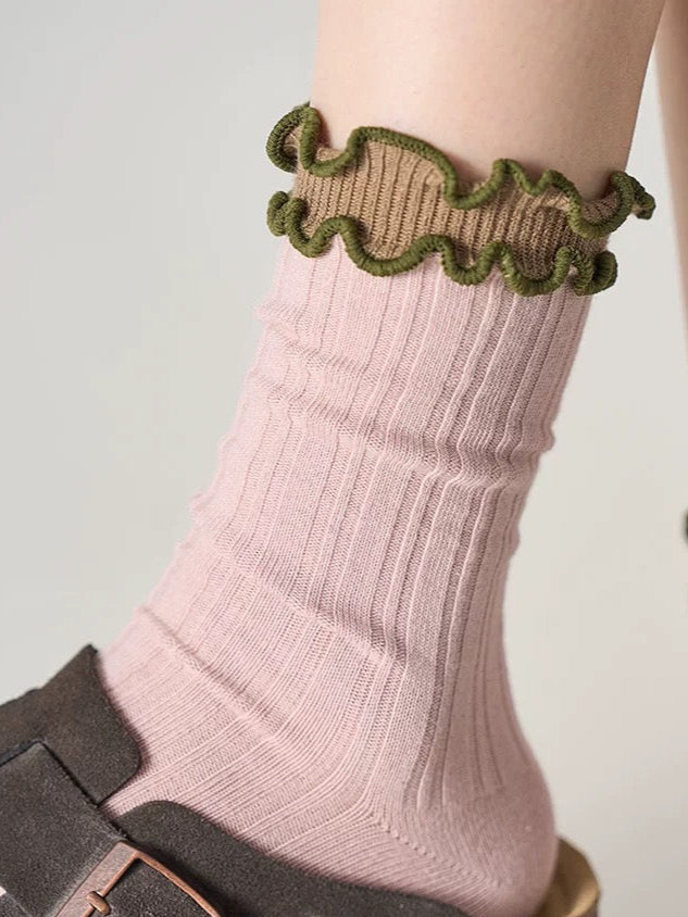Pink sock with green ruffled top worn by a person on a light gray background