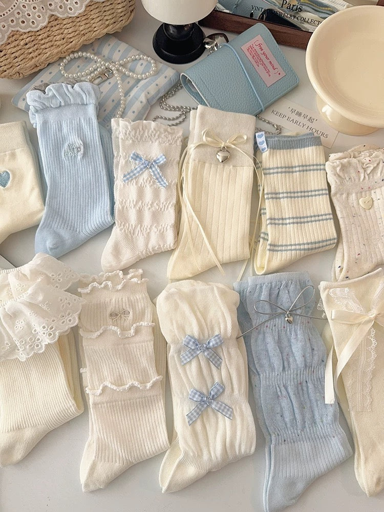 Collection of baby socks and booties on a light surface with a lamp and basket in the background.