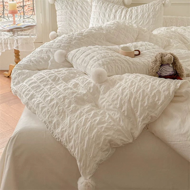 White textured comforter with pom-poms on a bed in a cozy bedroom.
