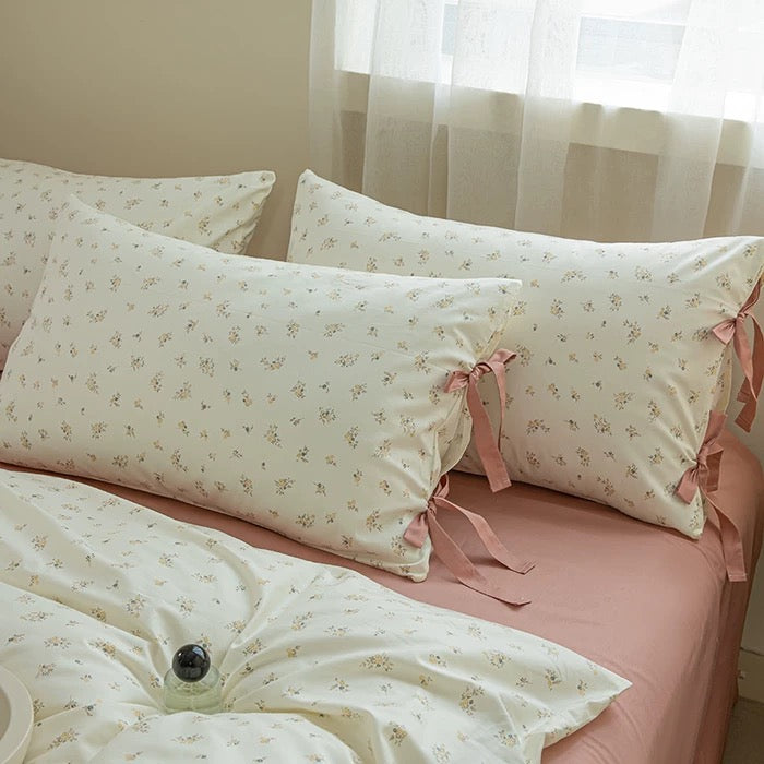 Floral patterned pillows with ribbons on a bed with pink bedding.