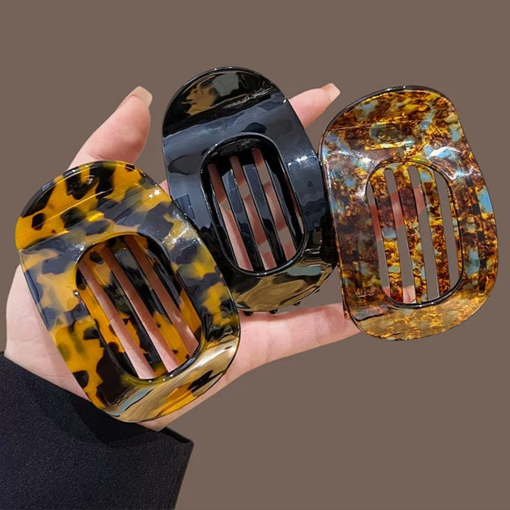 Three tortoiseshell patterned hair clips held in a hand against a brown background.