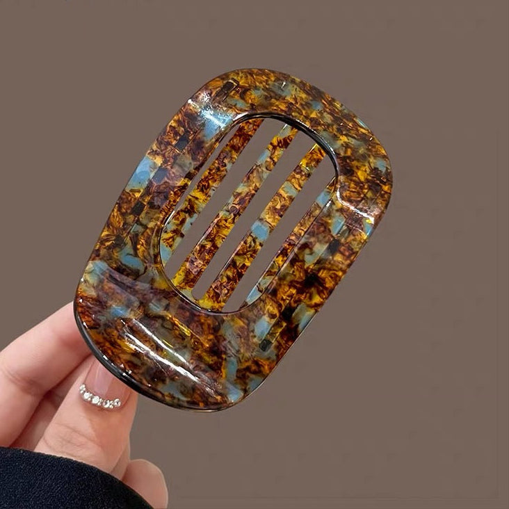 Hand holding a tortoiseshell patterned hair clip against a brown background