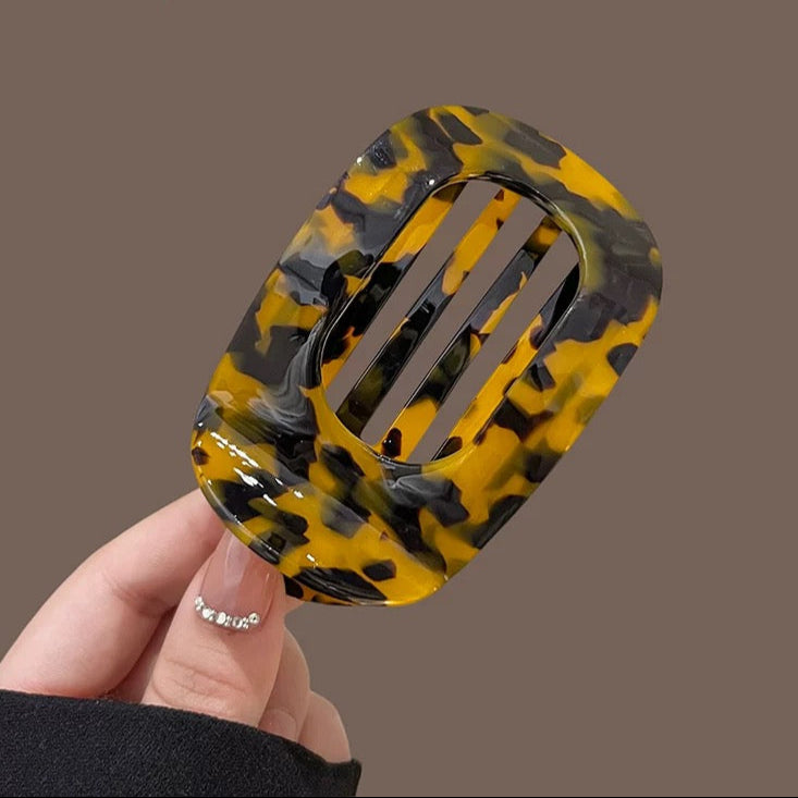 Hand holding a yellow and black patterned hair clip against a brown background