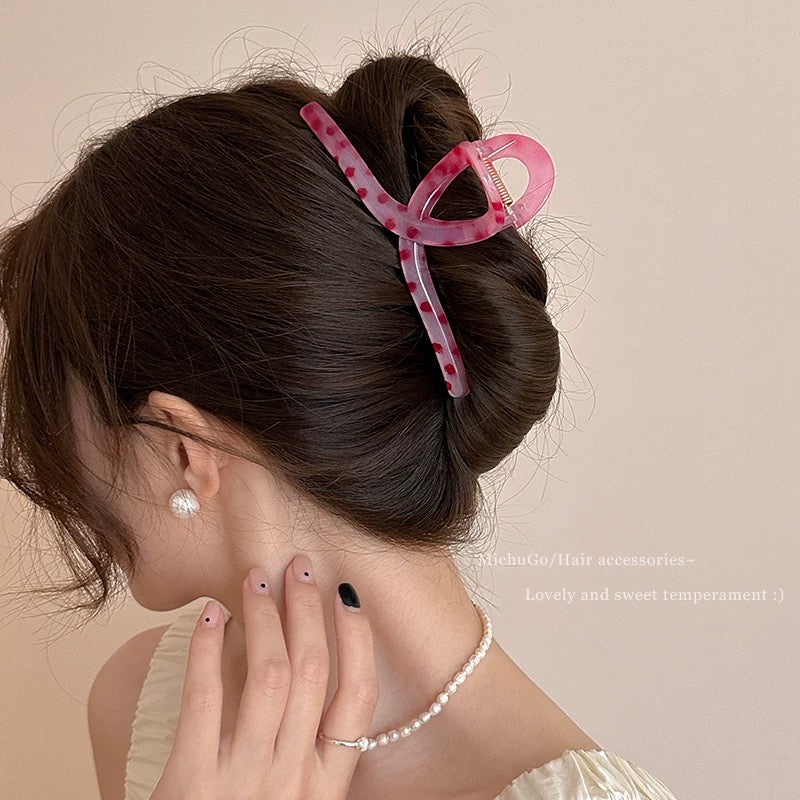 Woman with a pink hair clip in her hair, wearing a pearl necklace and earrings on a beige background.