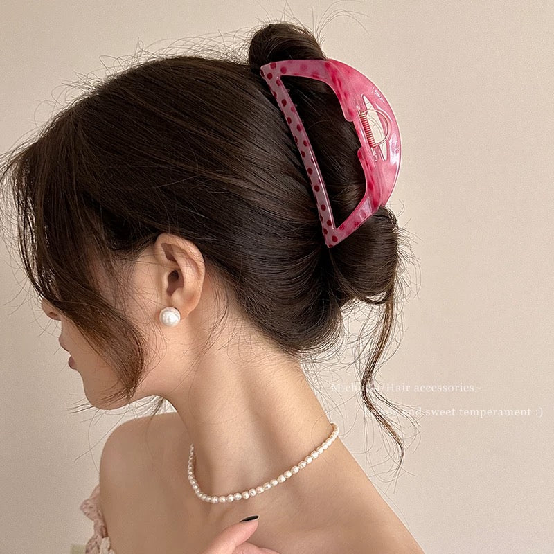 Woman with a pink hair clip in her hair, wearing a pearl necklace on a beige background