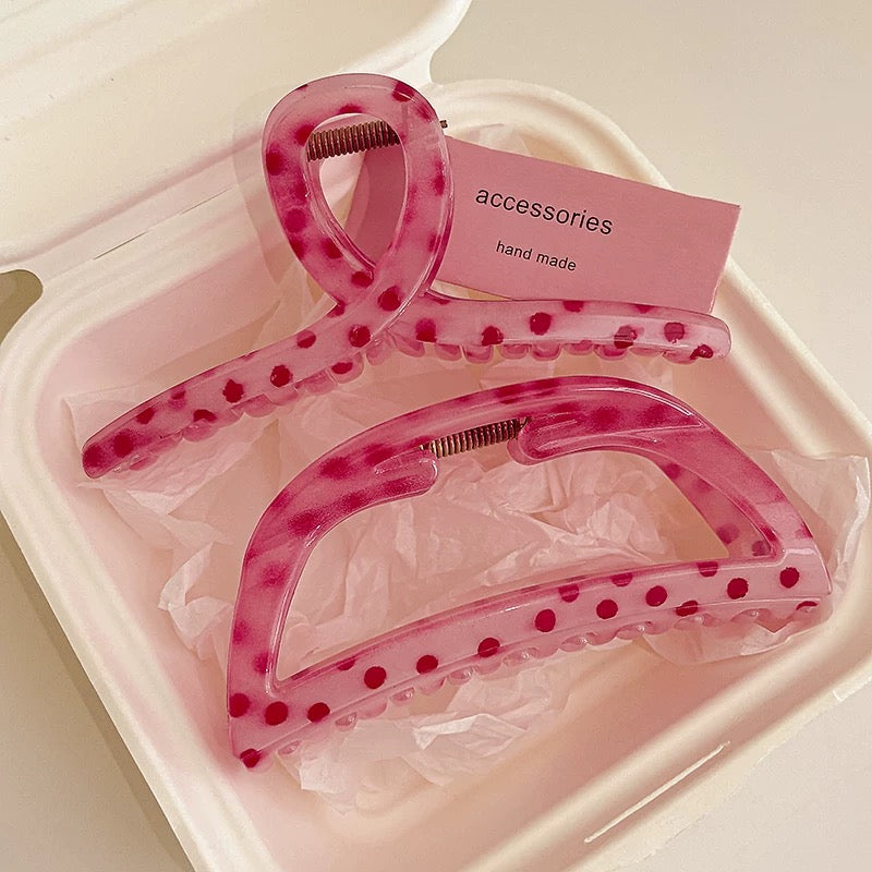 Pink hair clips with polka dots in a clear plastic case on a light pink background.