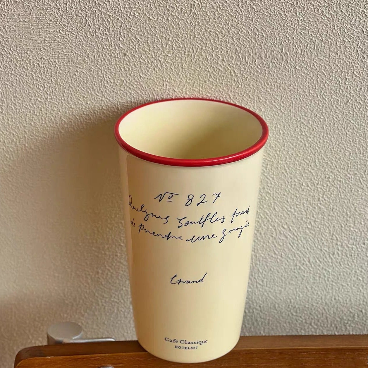 White tumbler with red rim on a wooden surface against a textured wall