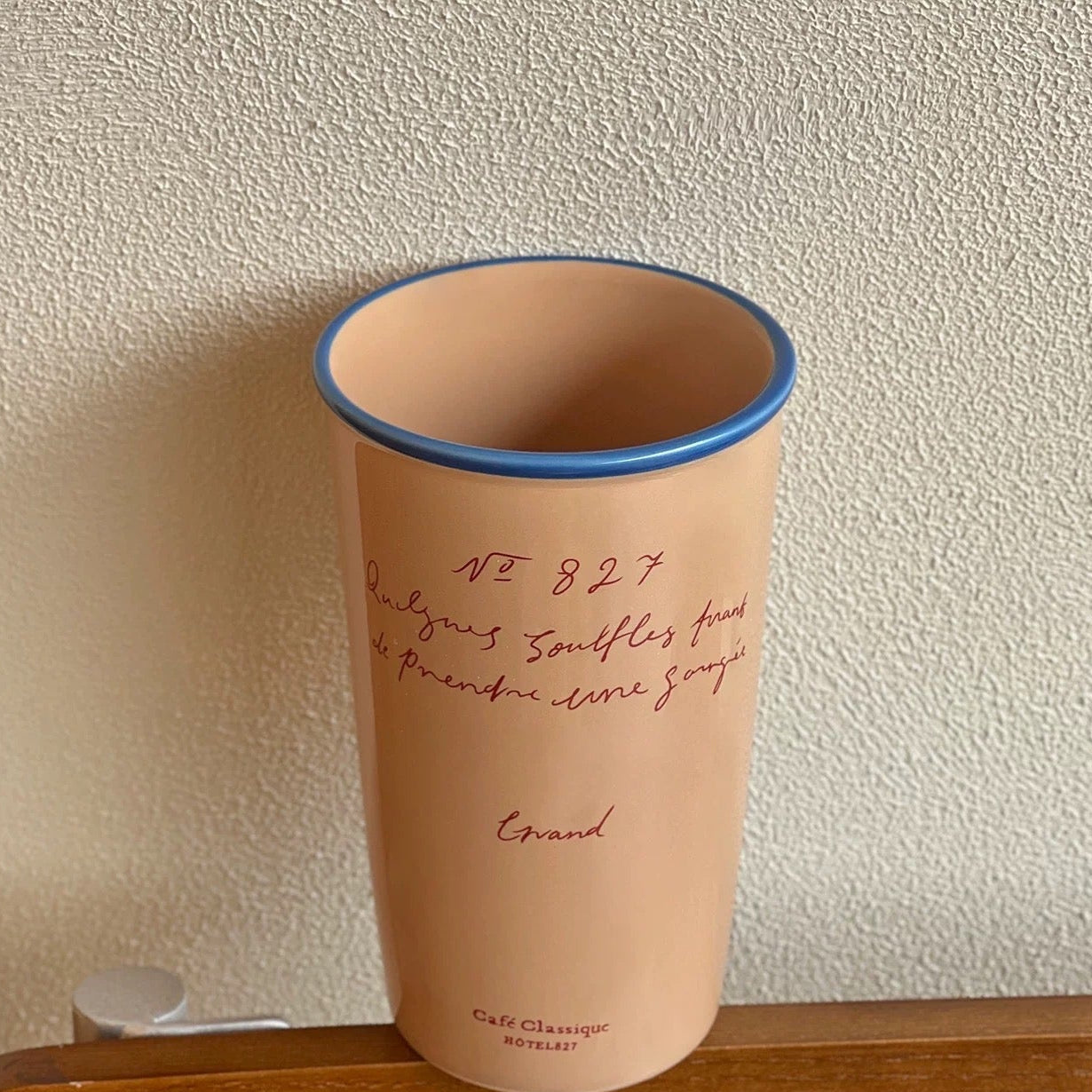 Beige tumbler with blue rim on a wooden surface against a beige wall