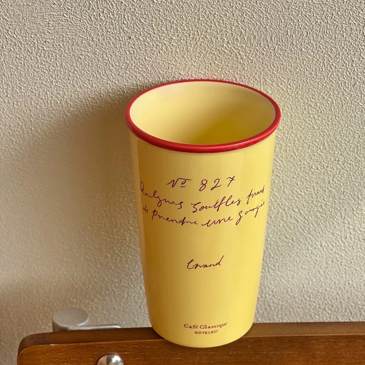 Yellow cup with red rim on a wooden surface against a textured wall