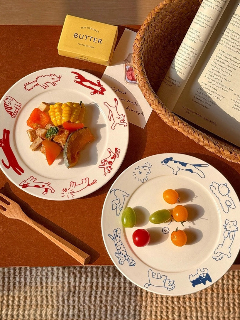 Two decorative plates with food on a wooden table, featuring an open book and a box of butter.