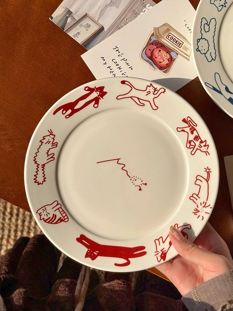 White plate with red cat illustrations held by a hand on a wooden surface.