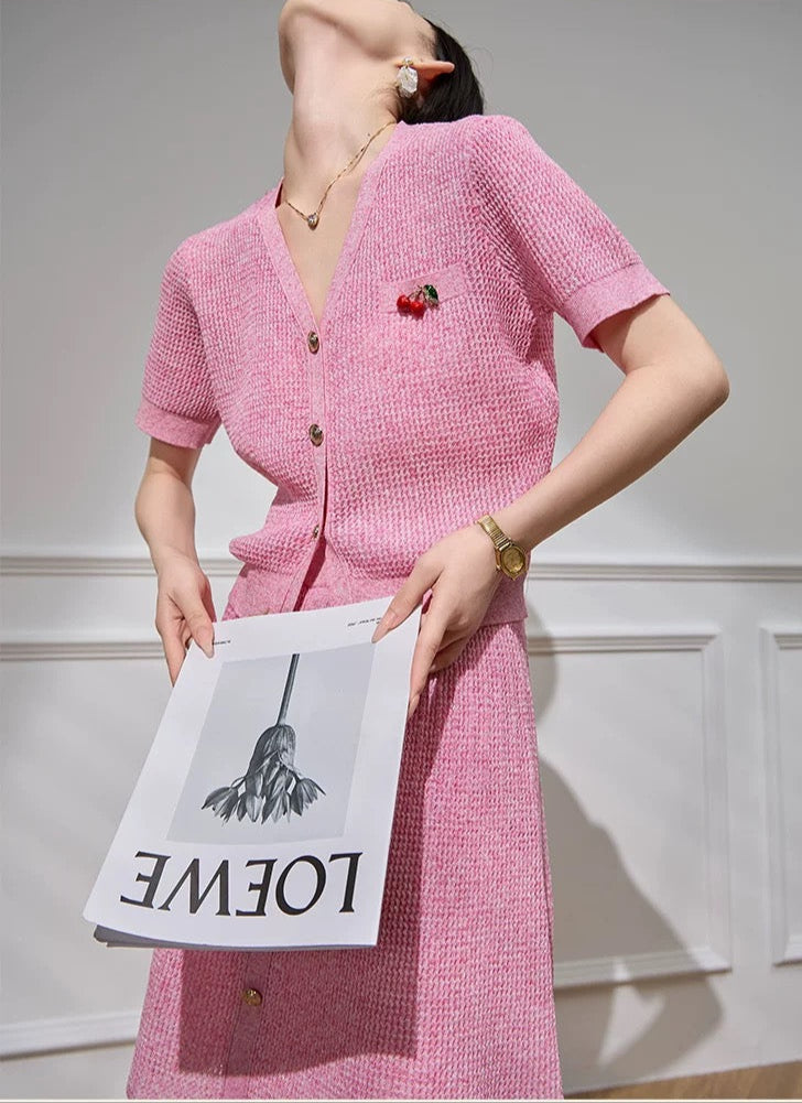 Person wearing a pink outfit holding a Loewe bag against a white wall.