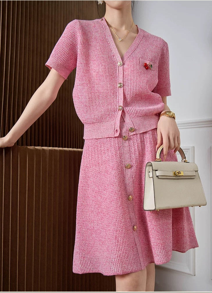 Woman wearing a pink outfit with a beige handbag, standing against a neutral background.
