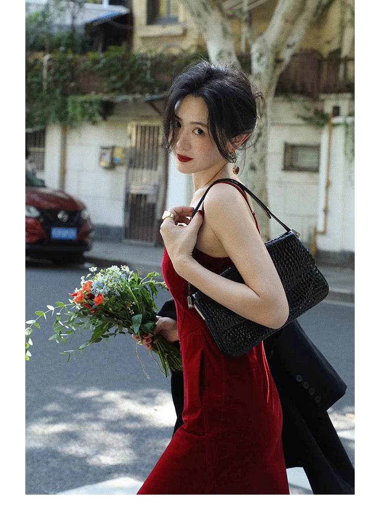 Woman in a red dress holding flowers and a black handbag on a street.