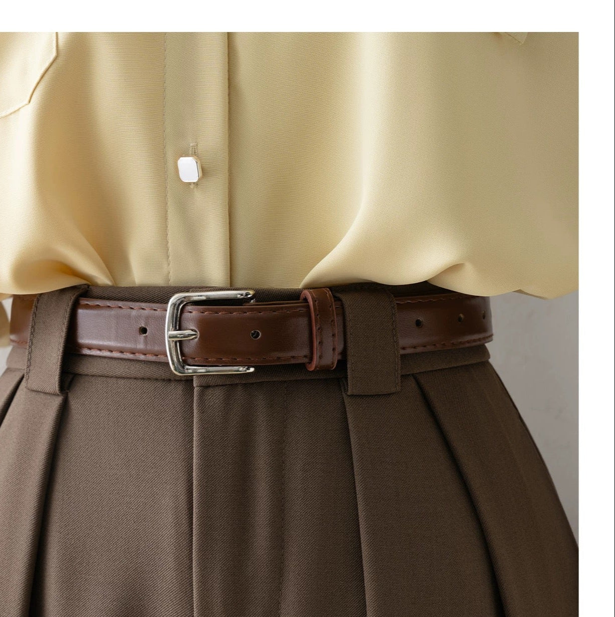 Beige shirt and brown pants with a belt on a plain background