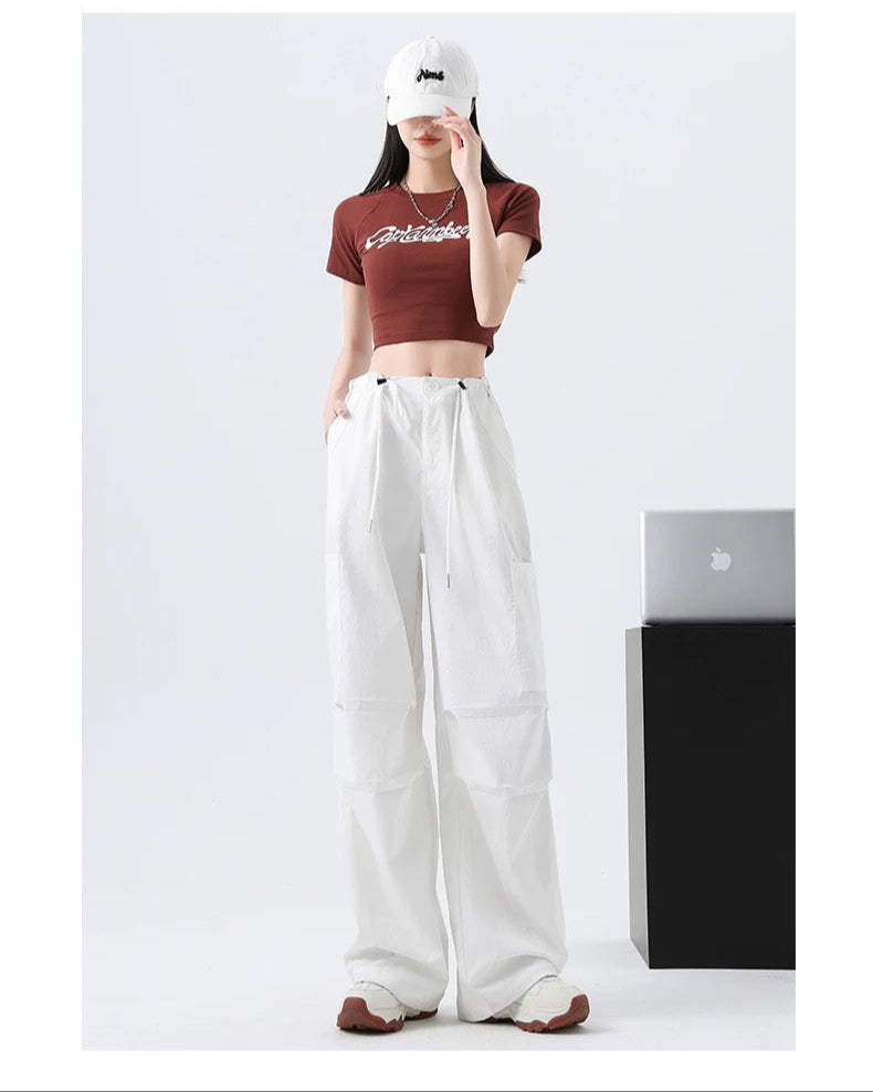 Person wearing a red crop top and white pants with a white cap, standing against a plain background.