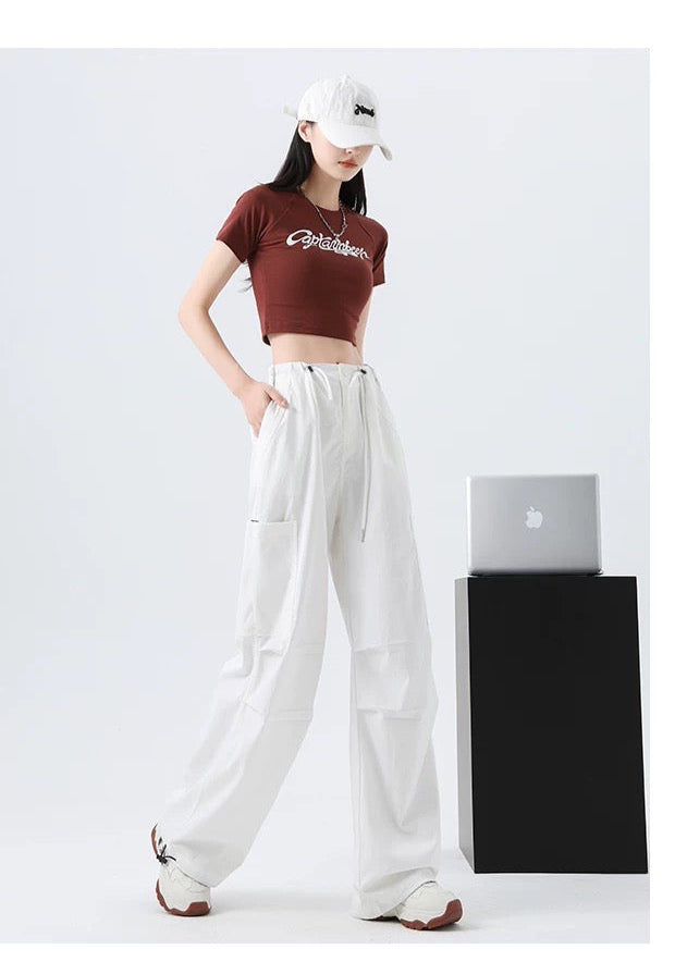 Person wearing a brown crop top and white pants standing next to a black box with a silver laptop on a white background