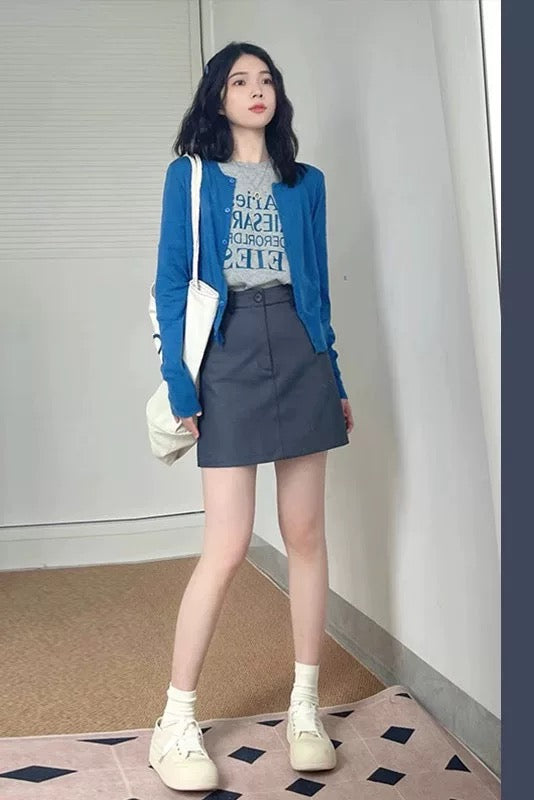 Woman wearing a blue cardigan and gray skirt with text on a white wall.