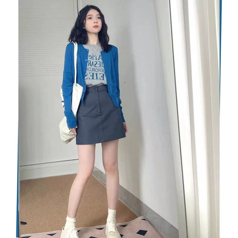 Woman wearing a blue jacket and gray skirt standing indoors with a white wall and carpeted floor.