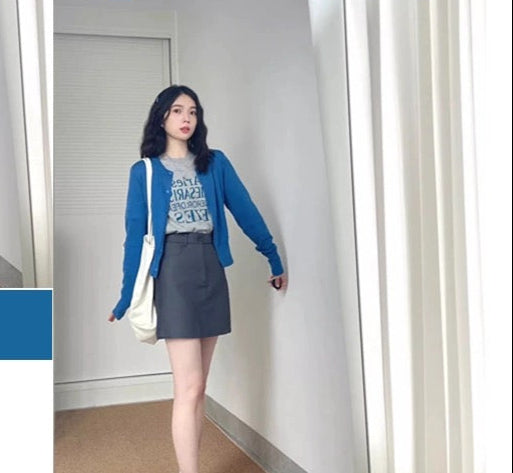 Woman wearing a blue cardigan and gray skirt in a room with white walls and a door.