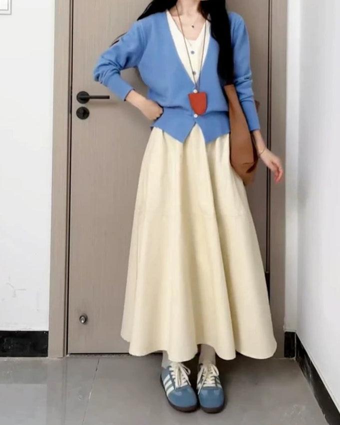 Person wearing, blue cardigan, and white skirt standing in a room.