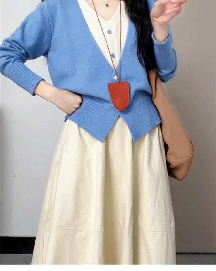 Person wearing a blue cardigan and beige skirt with a pig mask on a plain background