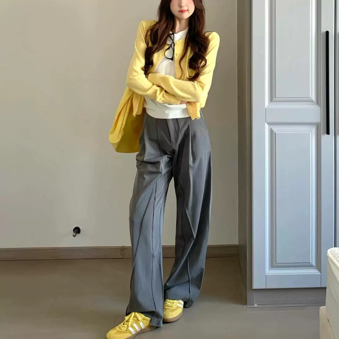 Woman wearing a yellow cardigan, white top, gray pants, and yellow shoes in a room.