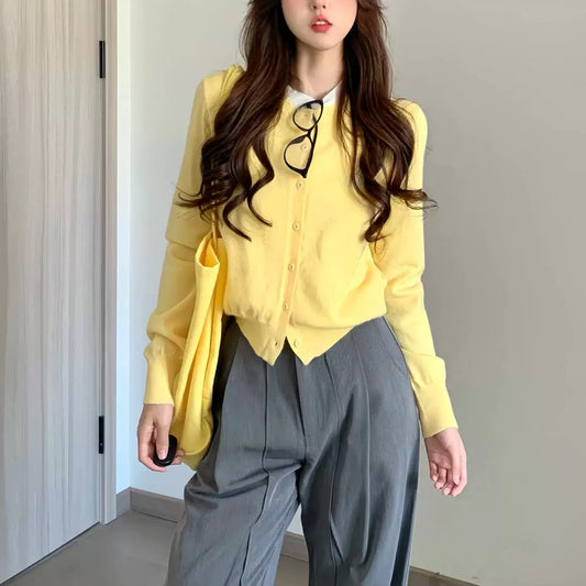 Woman wearing a yellow cardigan and gray pants indoors.