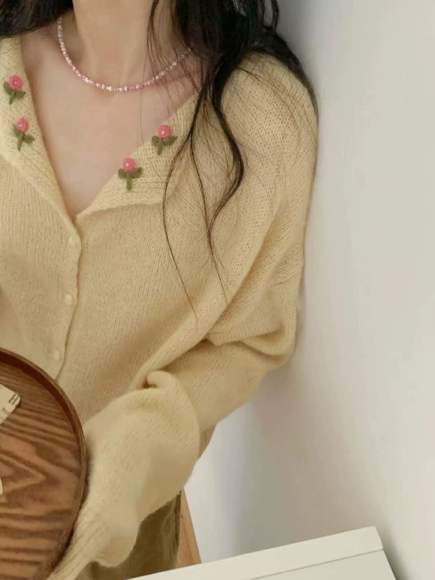 Woman wearing a beige cardigan with floral embellishments against a white background