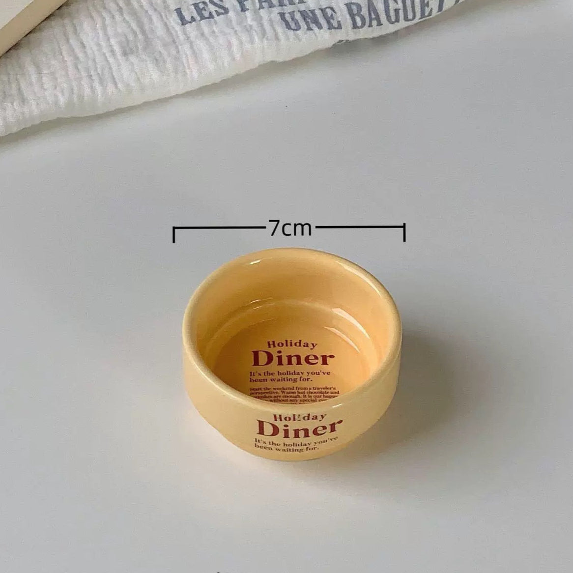 Small beige bowl with text on a white surface, showing measurement details.