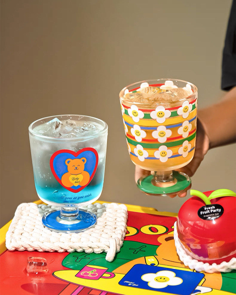 Two colorful glasses on a table with a child's coloring book underneath.