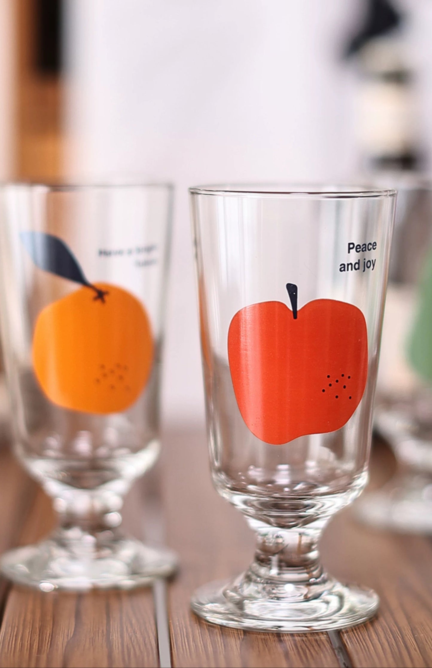 Clear glasses with orange and red apple designs on a wooden surface
