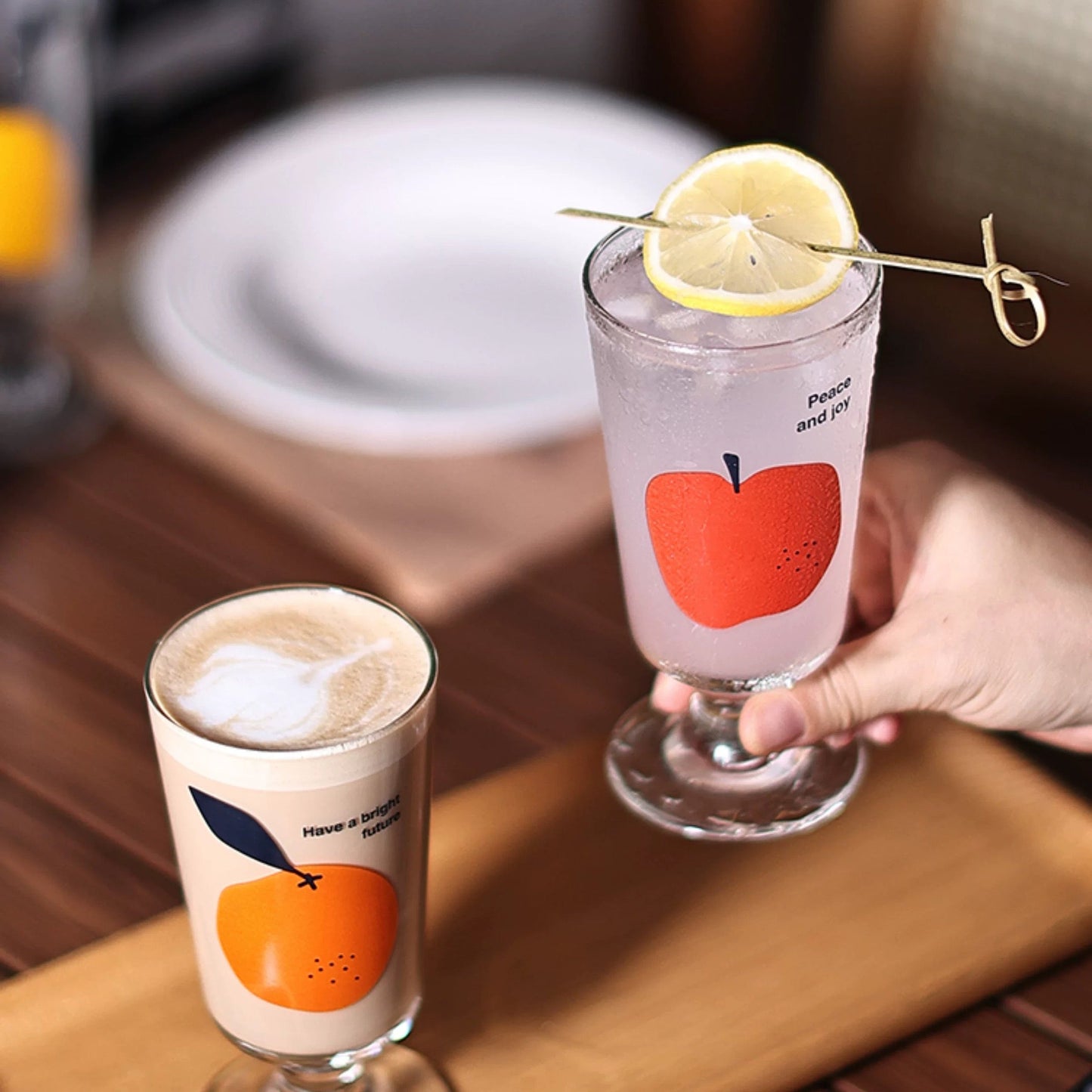 Two glasses of drinks with fruit-themed designs on a wooden table.
