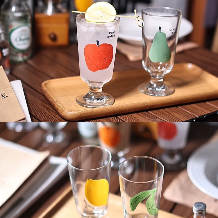 Two glasses with fruit-shaped ice cubes on a wooden tray.