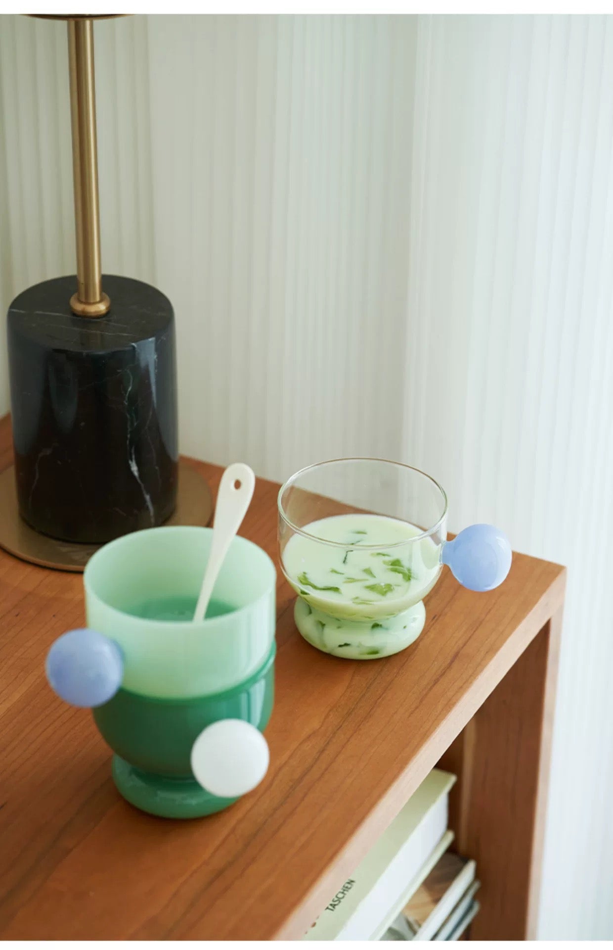 Green glass with white polka dots on a wooden surface next to a lamp.