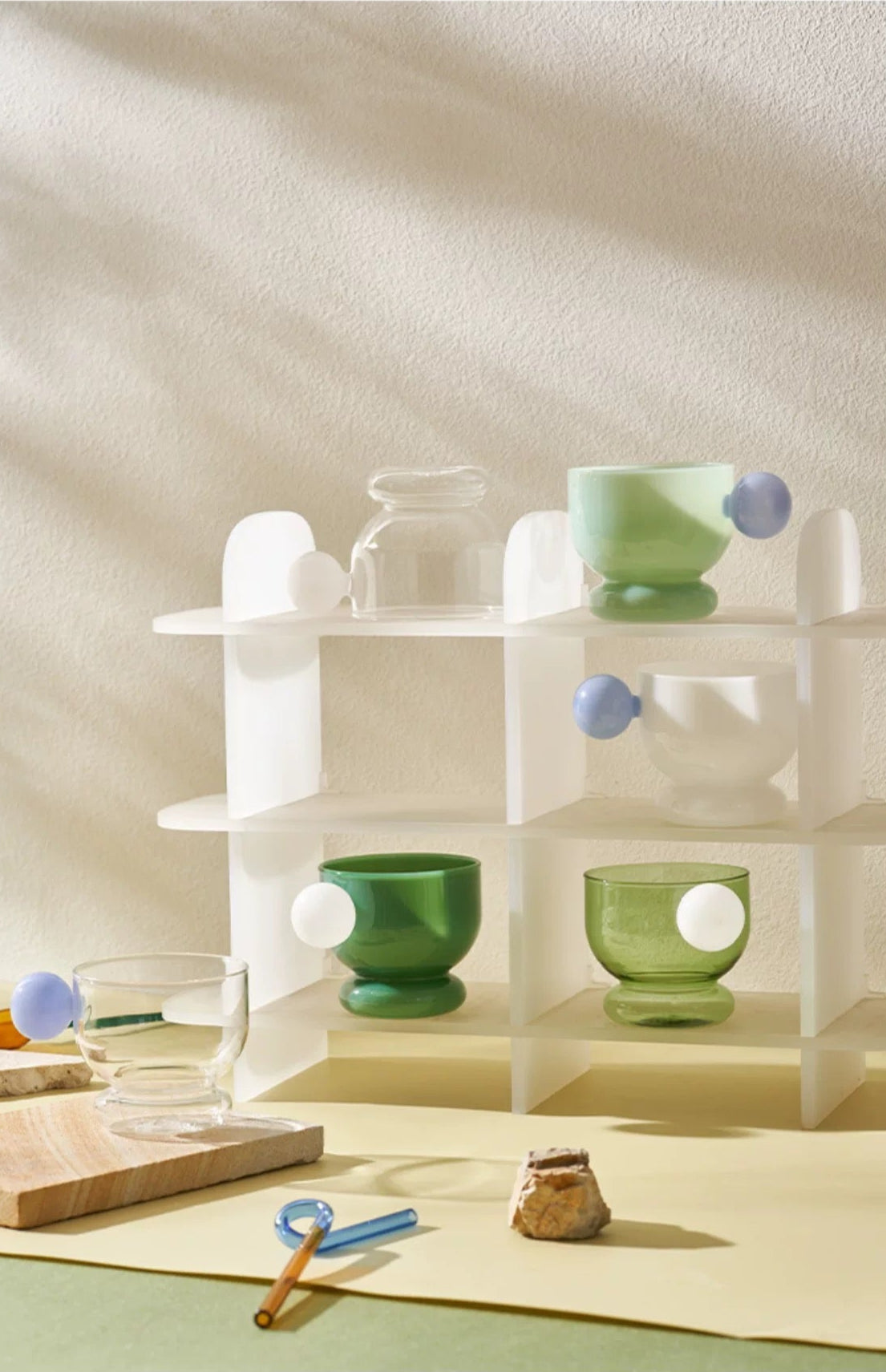 Set of green glass bowls on a white shelf against a light beige background